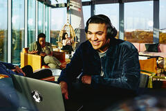 male sitting in a cafe working on his laptop smiling